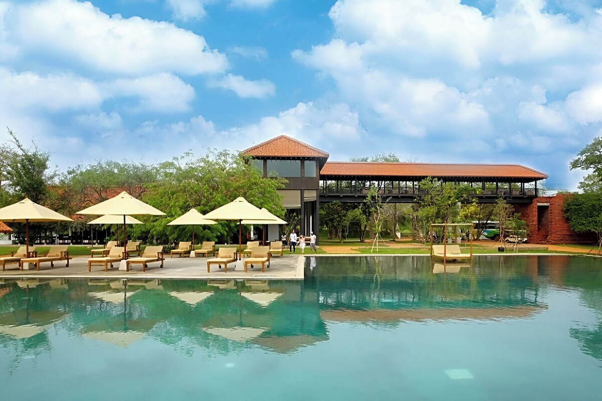 A swimming pool with lounge chairs and umbrellas, a building with a red roof, and a clear blue sky.
