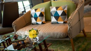 A modern living room with a green sofa, patterned cushions, a glass coffee table with books and a vase of flowers.
