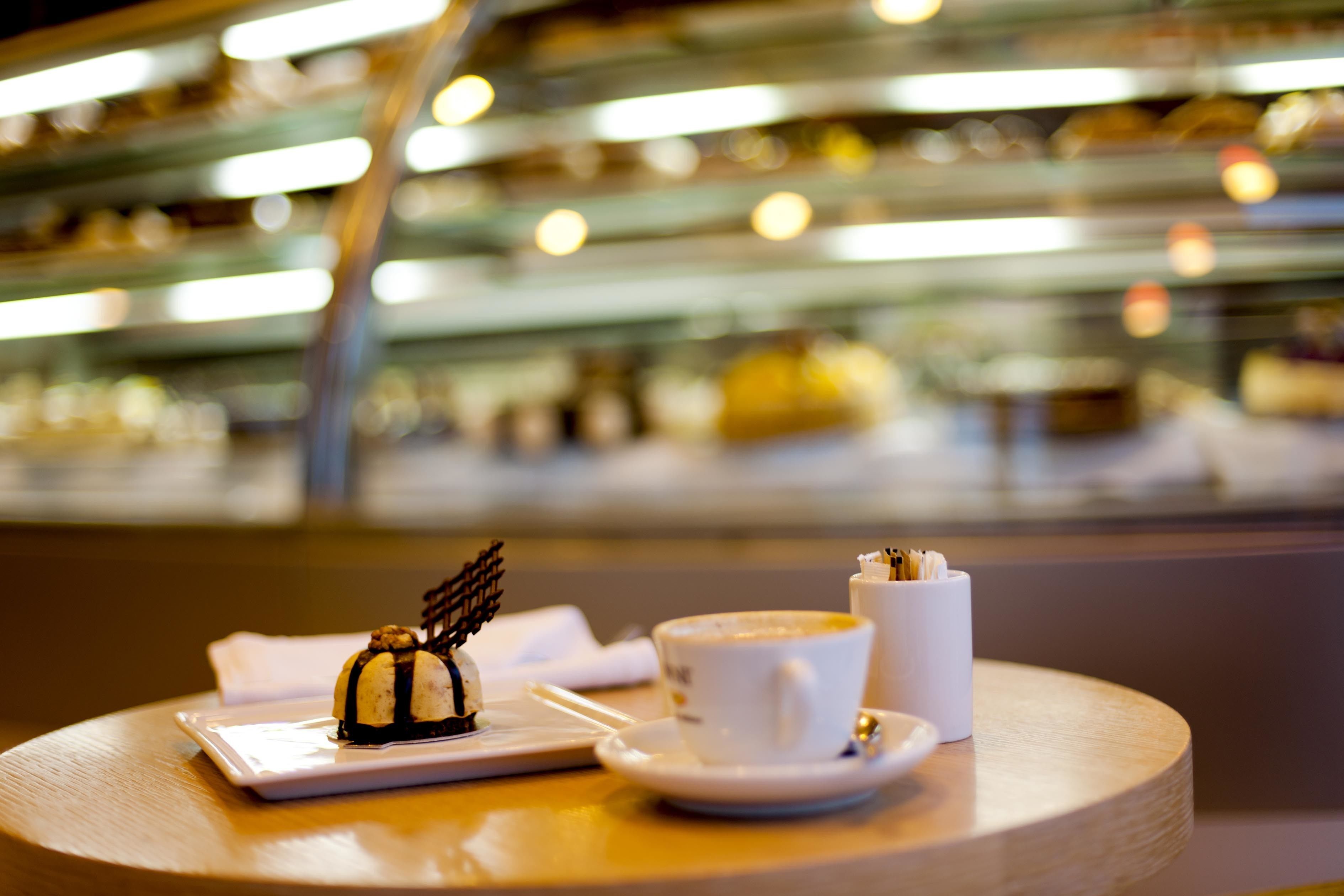 Een dessert op een tafel, met een kop koffie en een klein bakje, in een goed verlichte kamer met een onscherpe achtergrond.