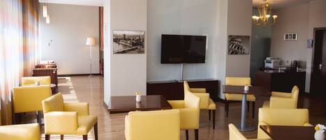 Un vestíbulo de hotel con sillas amarillas, un televisor de pantalla plana grande y suelo de madera.