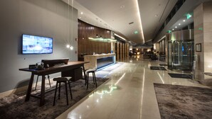 A modern hotel lobby with a reception desk, seating area, and a large TV screen.