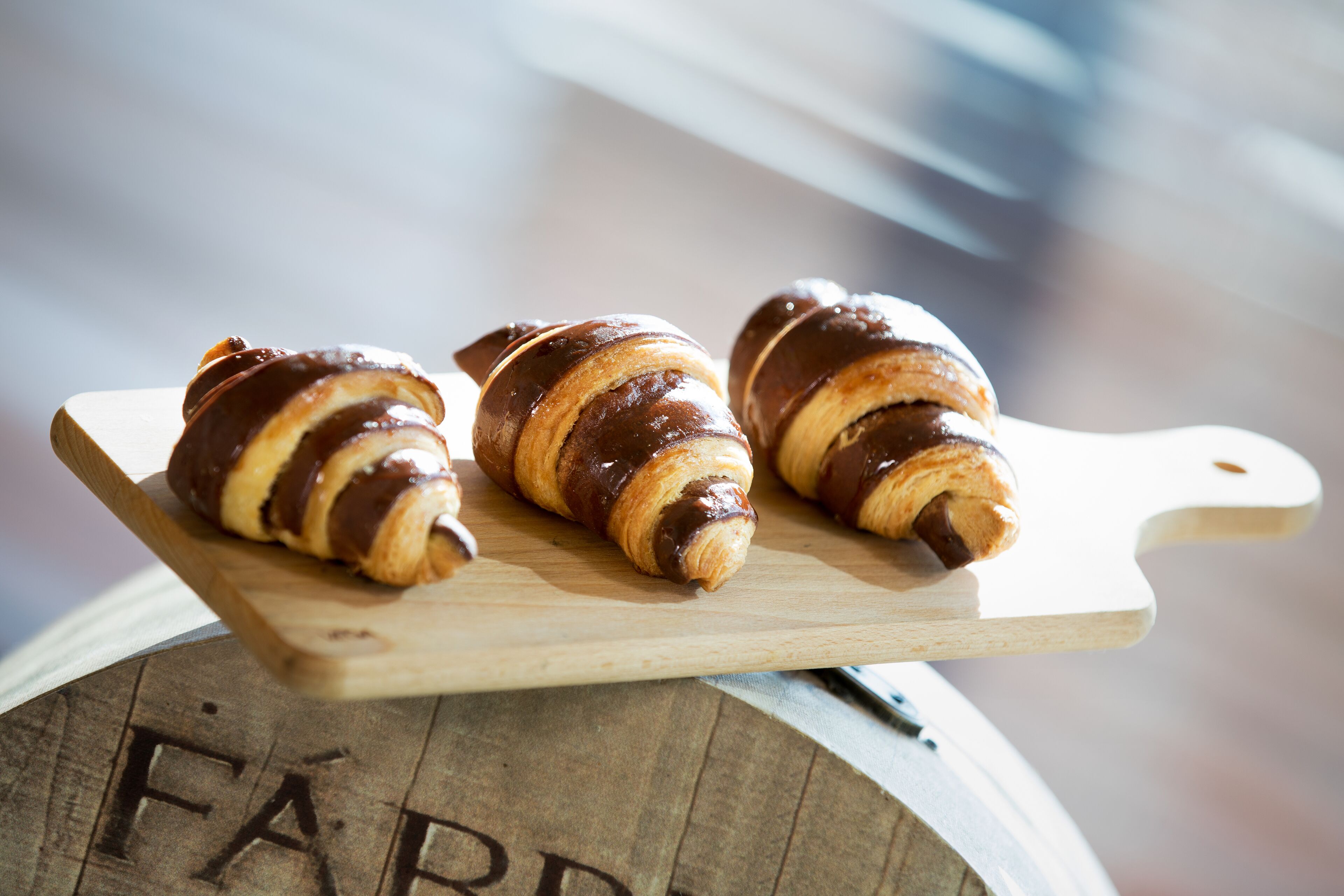 Three chocolate-covered croissants on a wooden cutting board.