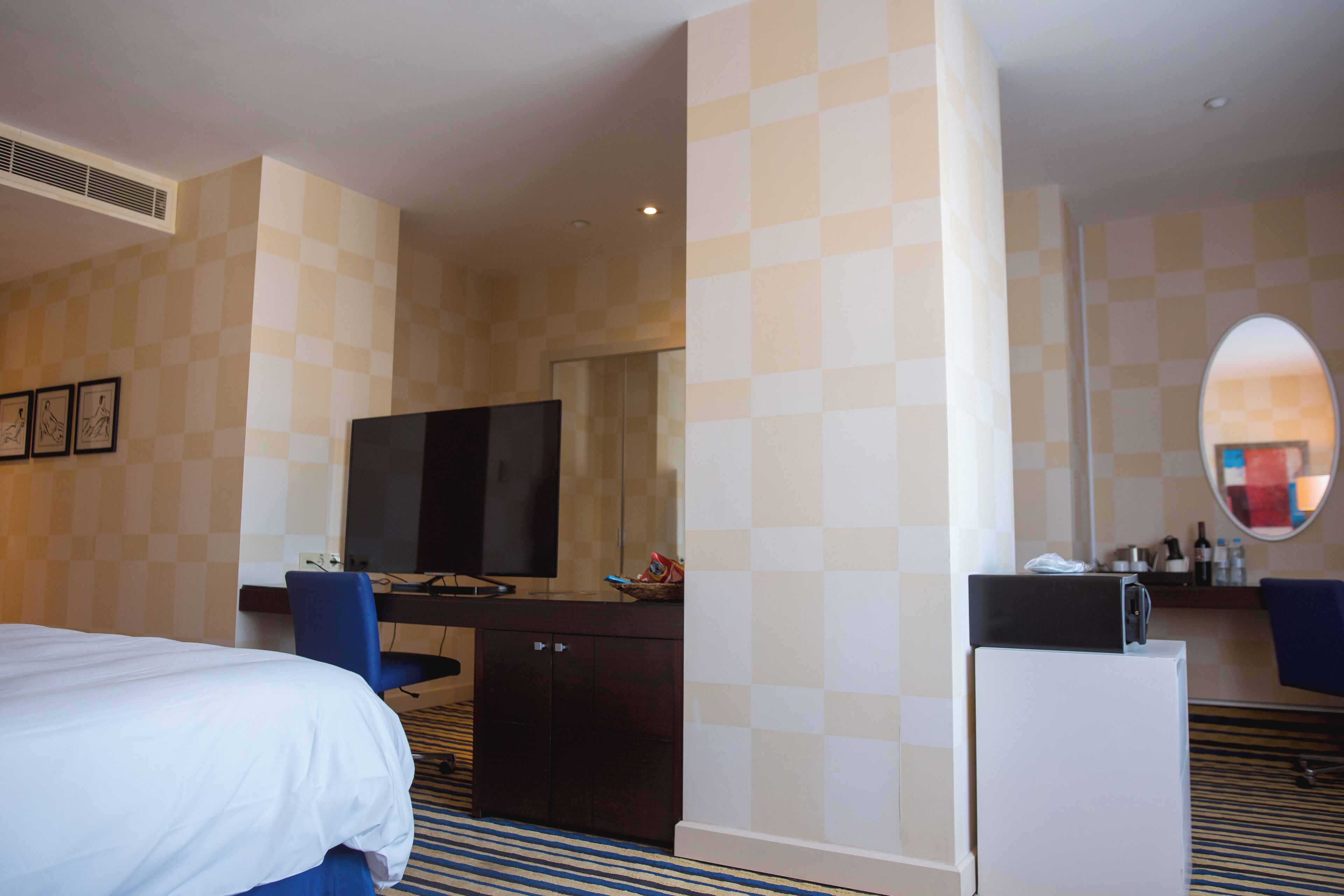 Ein Hotelzimmer mit einem Bett, einem Schreibtisch, einem Fernseher, einem Kühlschrank und einem Spiegel.