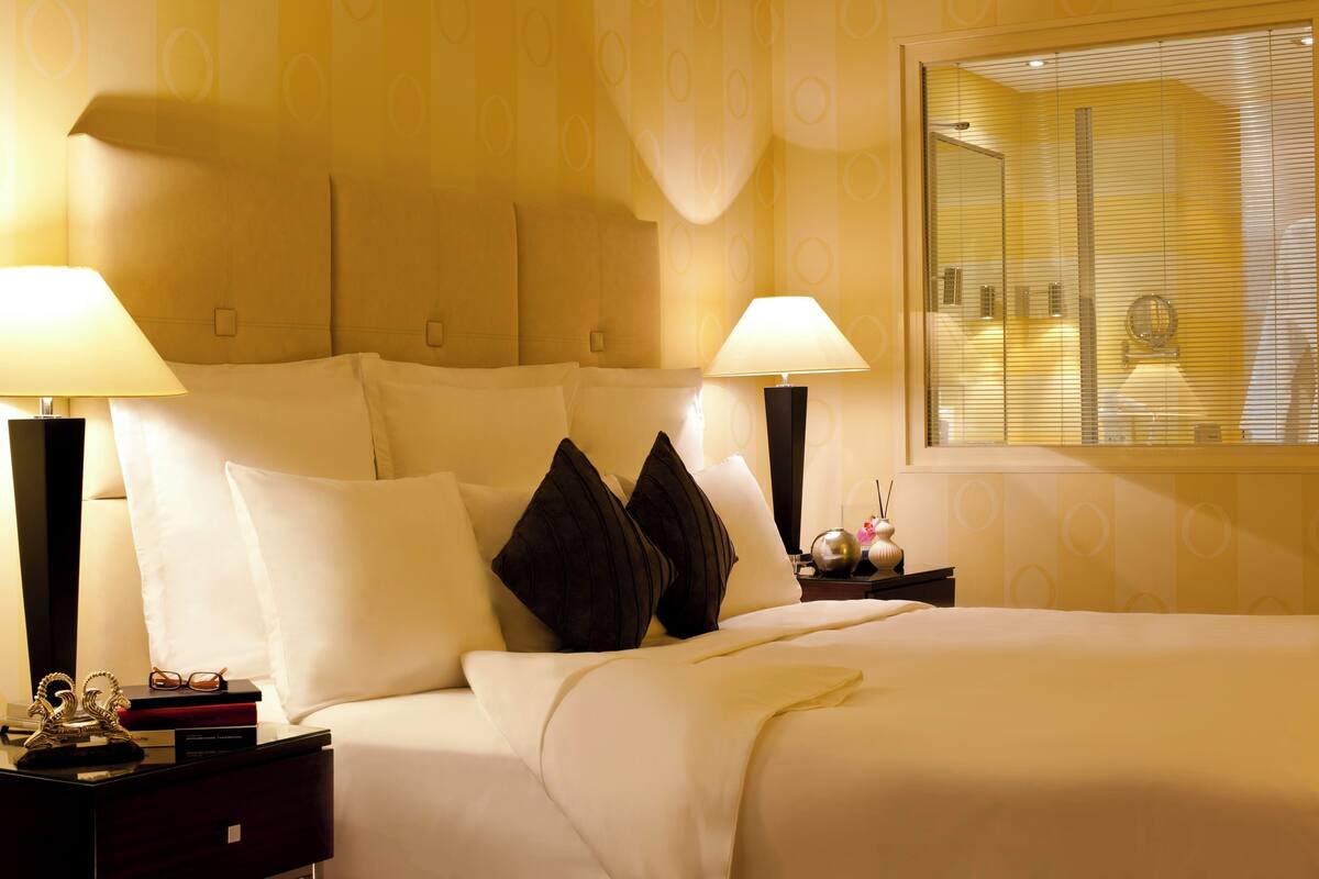 A hotel room with a large bed, two bedside lamps, a nightstand with a lamp, a mirror, and a window with blinds.