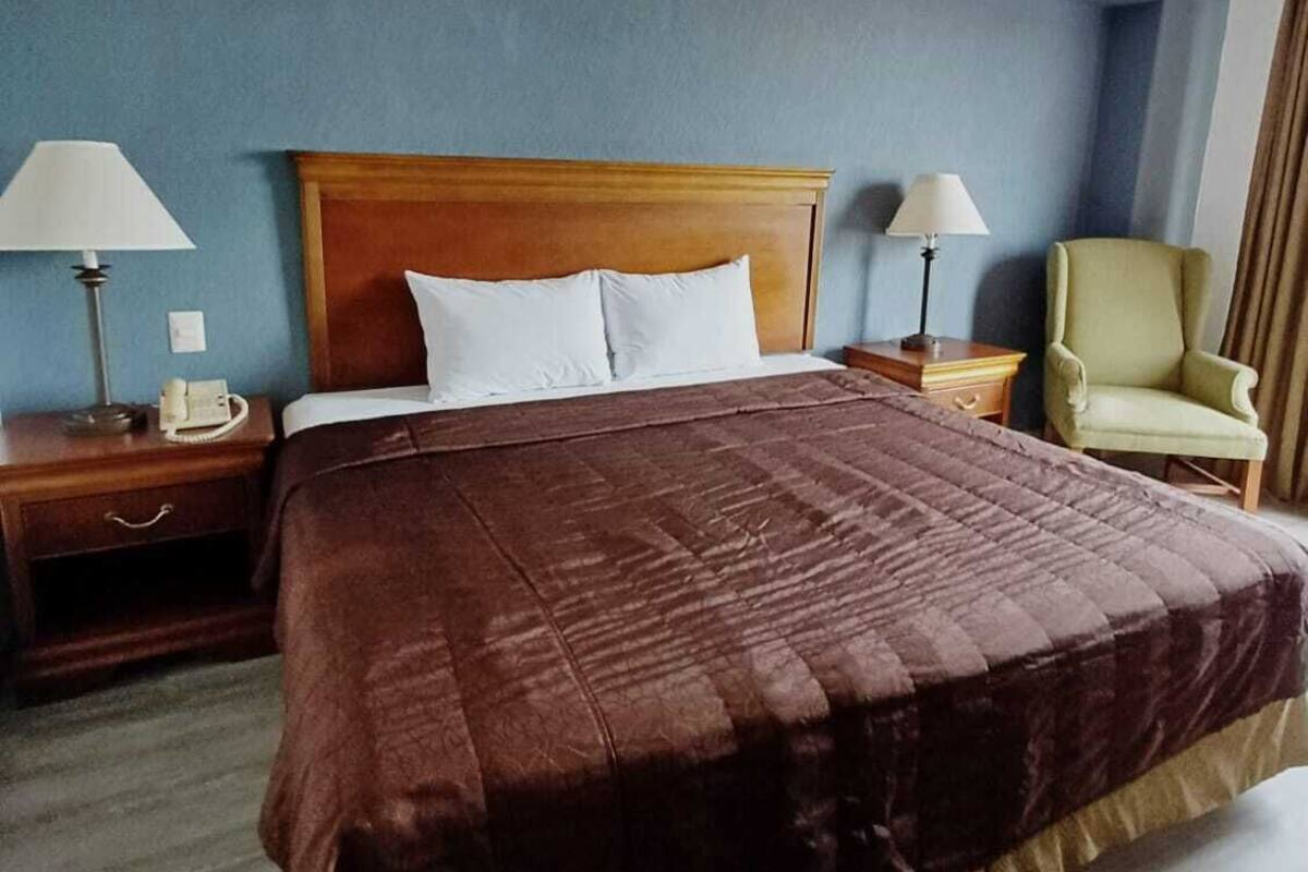 Habitación de hotel con una cama grande, dos mesitas de noche con lámparas, una silla y una pared azul.