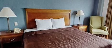 A hotel room with a large bed, two bedside tables with lamps, a chair, and a blue wall.