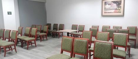 A conference room with rows of green upholstered chairs, a central table, and a framed picture on the wall.