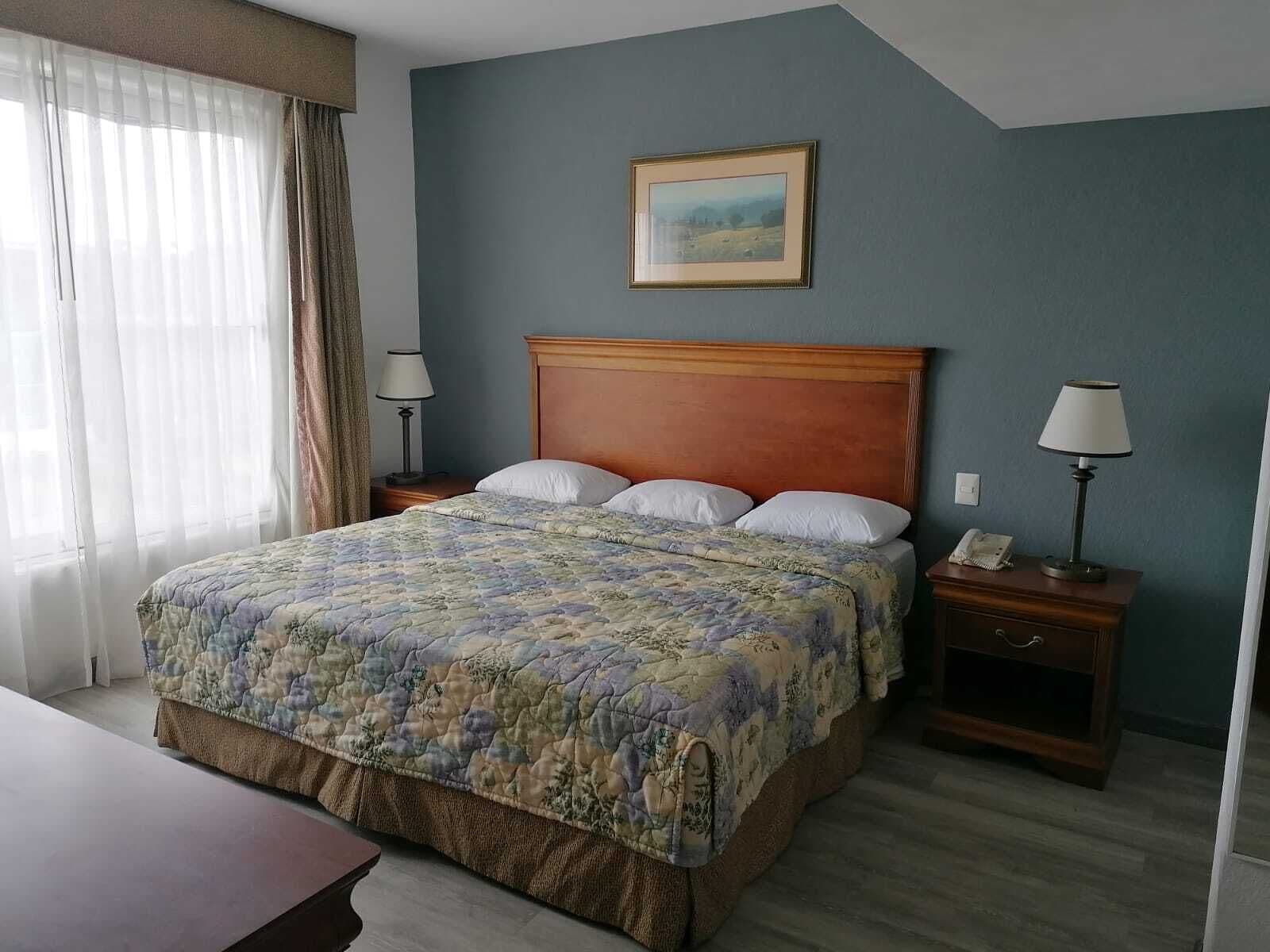Una habitación de hotel con una cama grande, dos mesitas de noche, un escritorio y una ventana con cortinas.