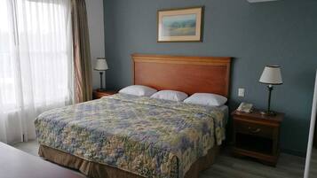 Una habitación de hotel con una cama grande, dos mesitas de noche, un escritorio y una ventana con cortinas.