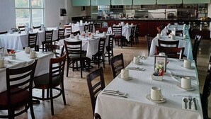 A restaurant with multiple tables set for dining, a kitchen area in the background, and large windows allowing natural light. - Sierra Huasteca Inn (Ciudad Valles)