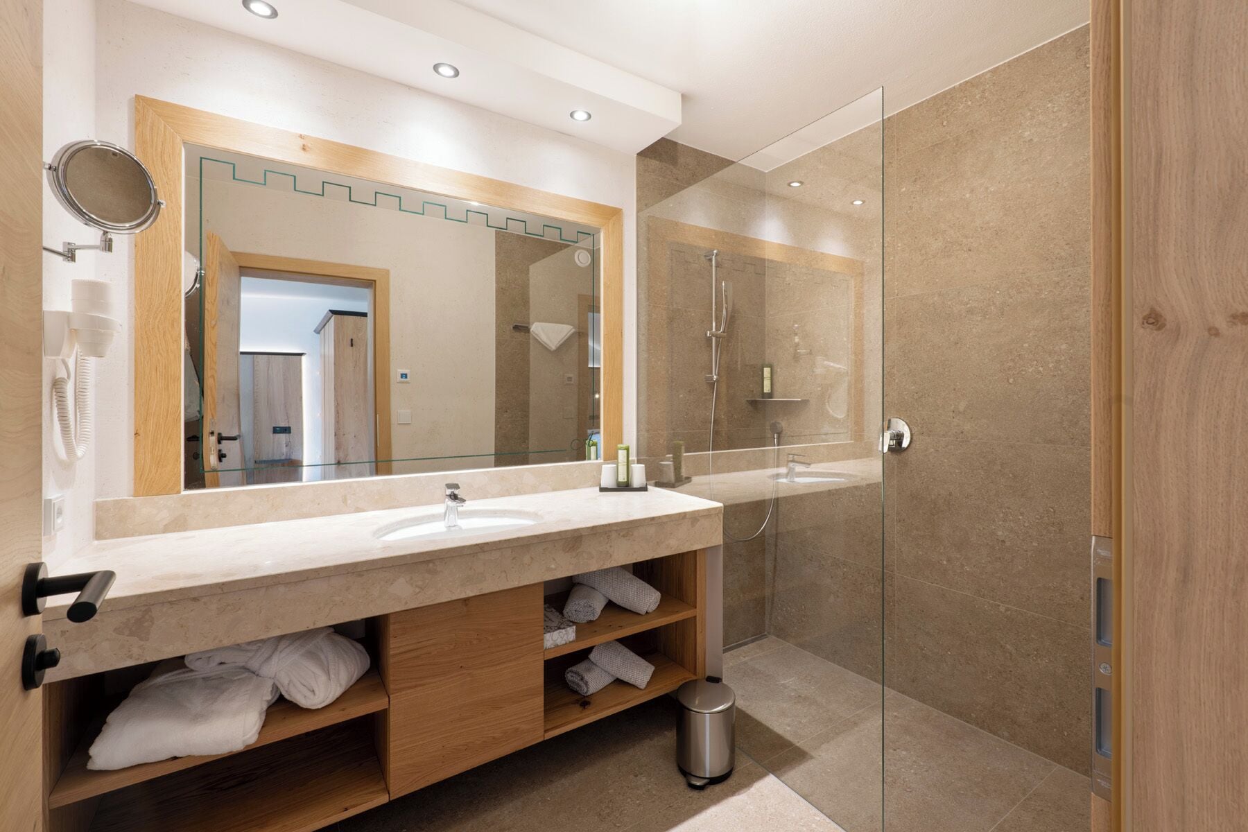A modern bathroom with a double sink vanity, a glass shower enclosure, and a mirror with a wooden frame.