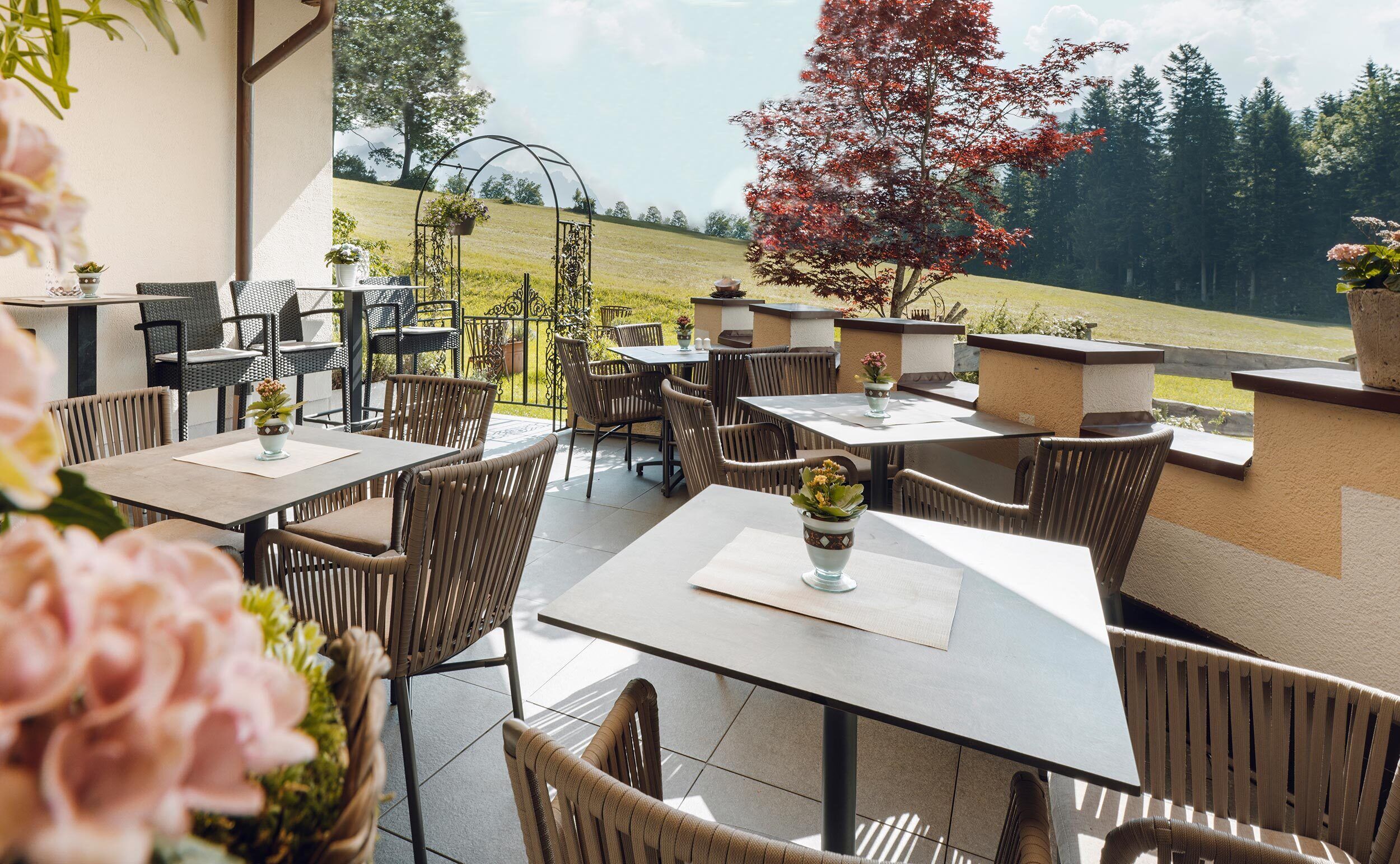 An outdoor patio area with multiple tables and chairs, surrounded by a low wall and potted plants.