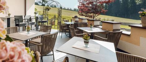 An outdoor patio area with multiple tables and chairs, surrounded by a low wall and potted plants.
