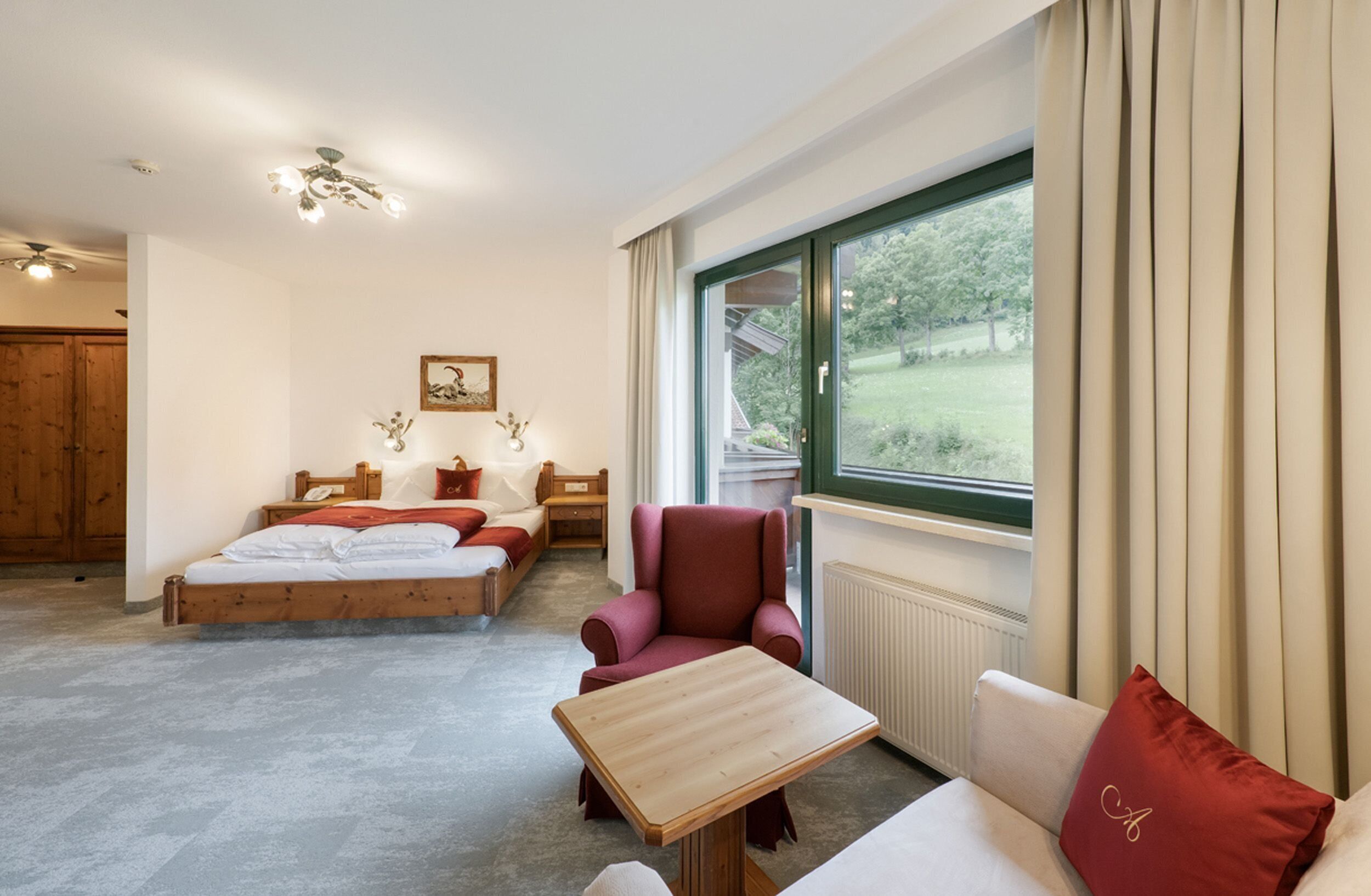 A bedroom with a bed, a chair, a table, and a window with curtains.