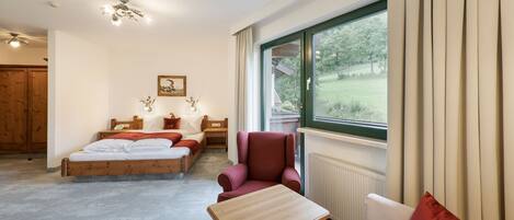 A bedroom with a bed, a chair, a table, and a window with curtains.