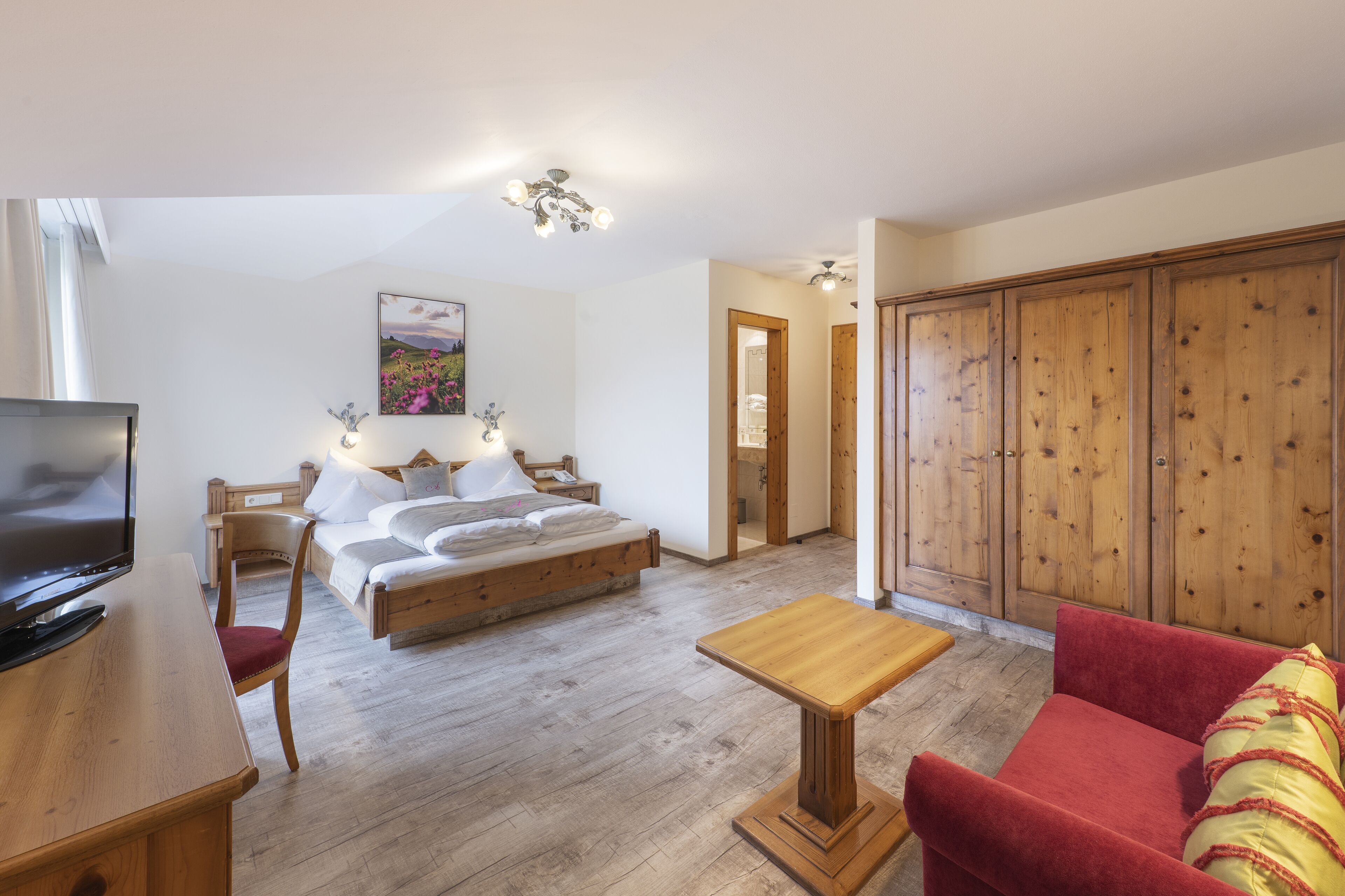 A bedroom with a bed, bedside table, TV, and a wooden wardrobe.