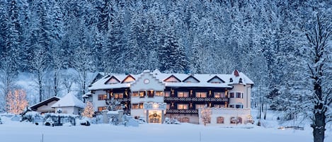 Un hotel grande de varios pisos con fachada cubierta de nieve, rodeado por un área boscosa.