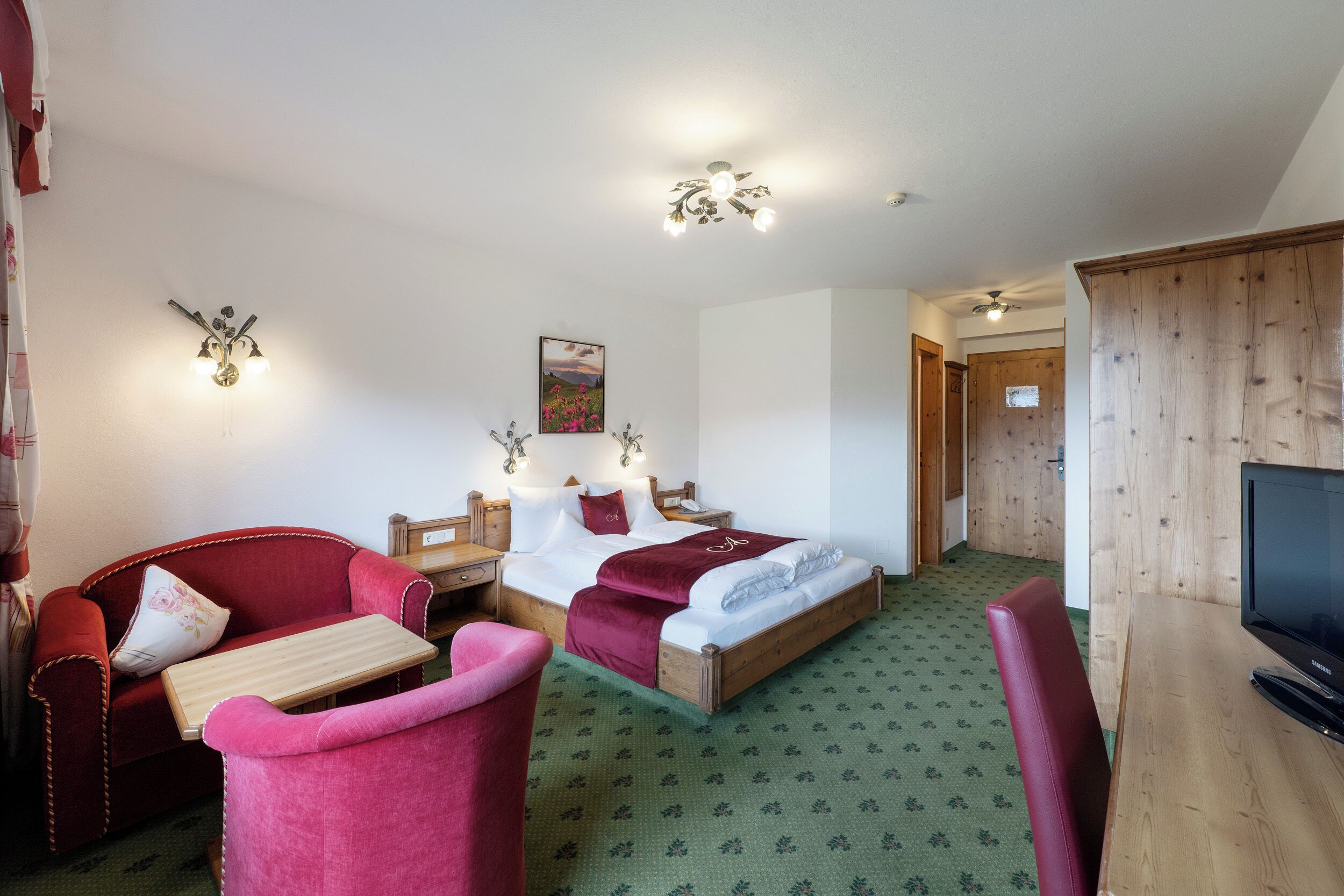 A hotel room with a bed, a desk, a chair, a television, and a door.
