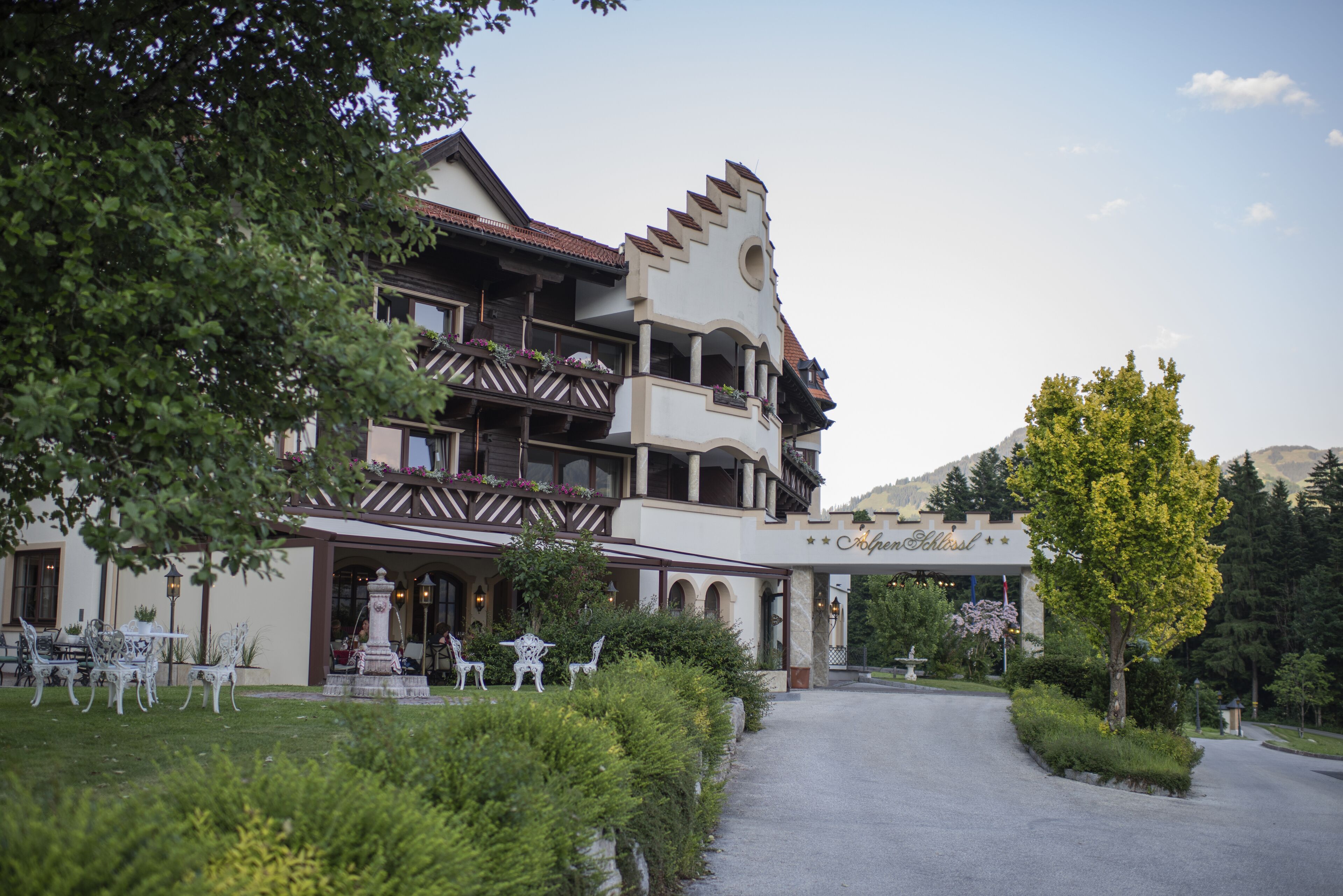 Ein mehrstöckiges Hotel mit Balkon, Springbrunnen und Garten.