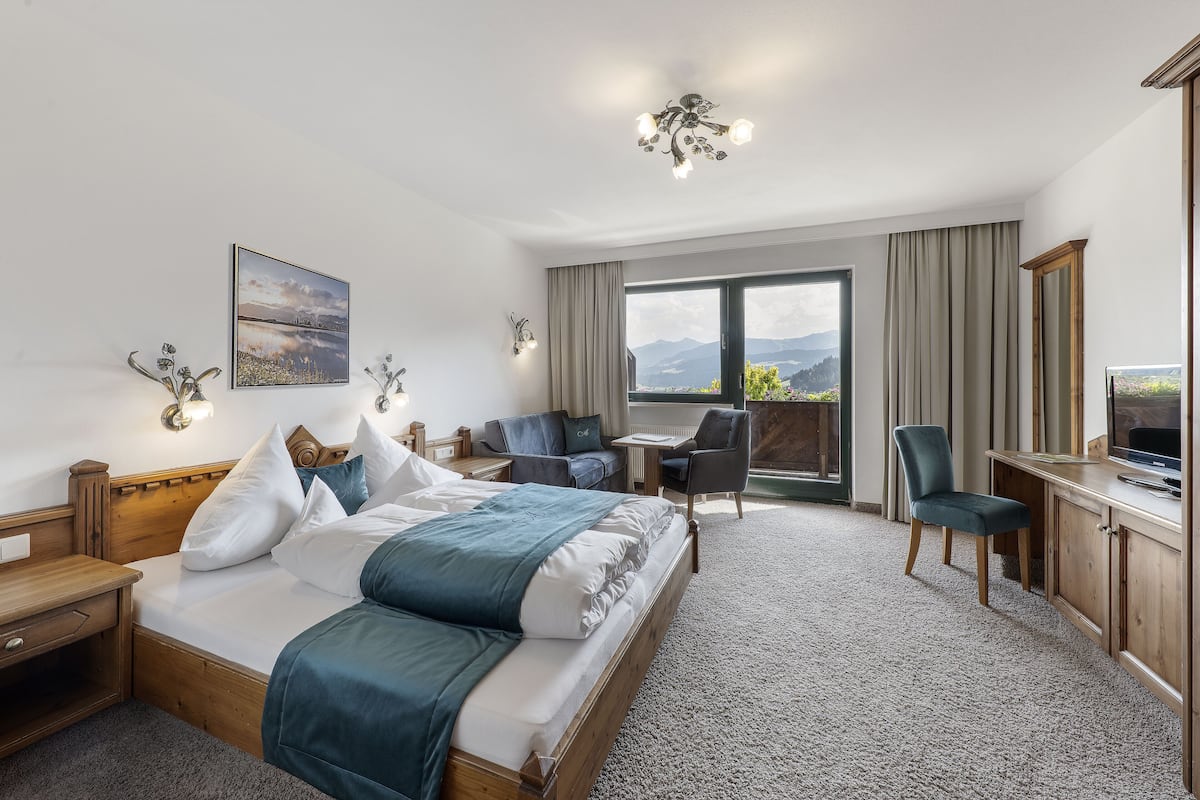 A hotel room with a large bed, a desk, a chair, a TV, and a window with a mountain view.