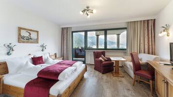 A hotel room with a bed, a desk, a chair, a TV, and a window with a mountain view.