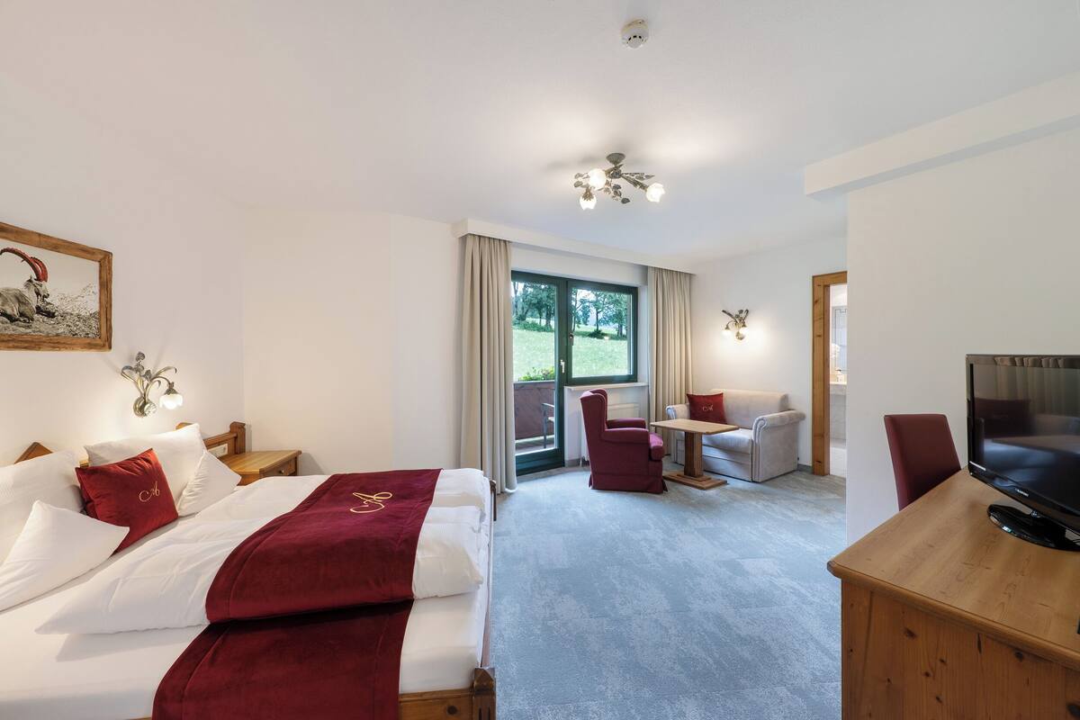 A hotel room with two beds, a desk, a TV, and a balcony with curtains.