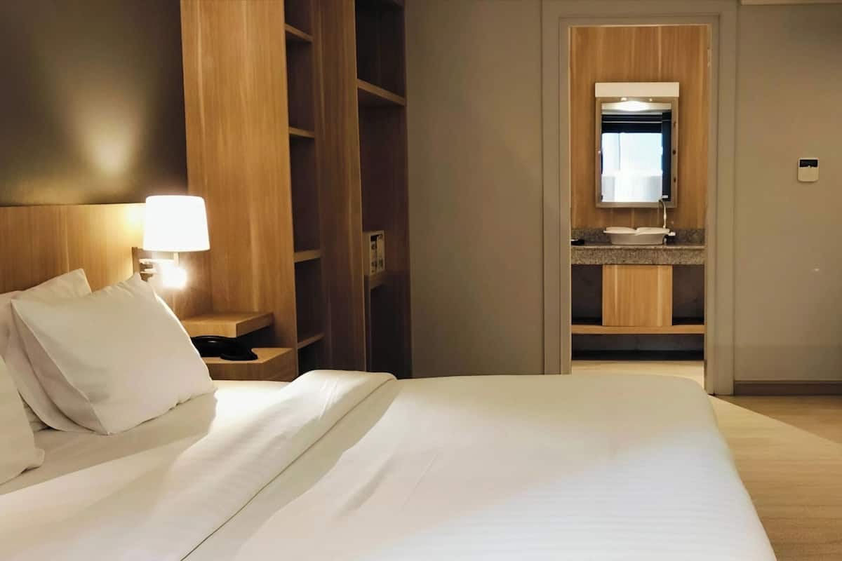 Een hotelkamer met een groot bed, een nachtkastje met lamp, een houten garderobe en een badkamer die door een open deur zichtbaar is.