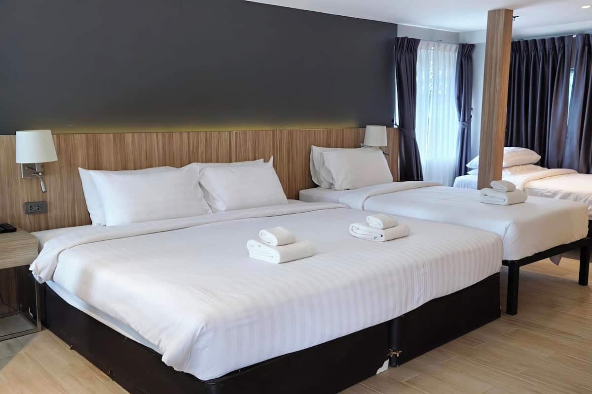 Hotelkamer met twee bedden, een houten hoofdbord, een nachtkastje met lamp en een raam met gordijnen.