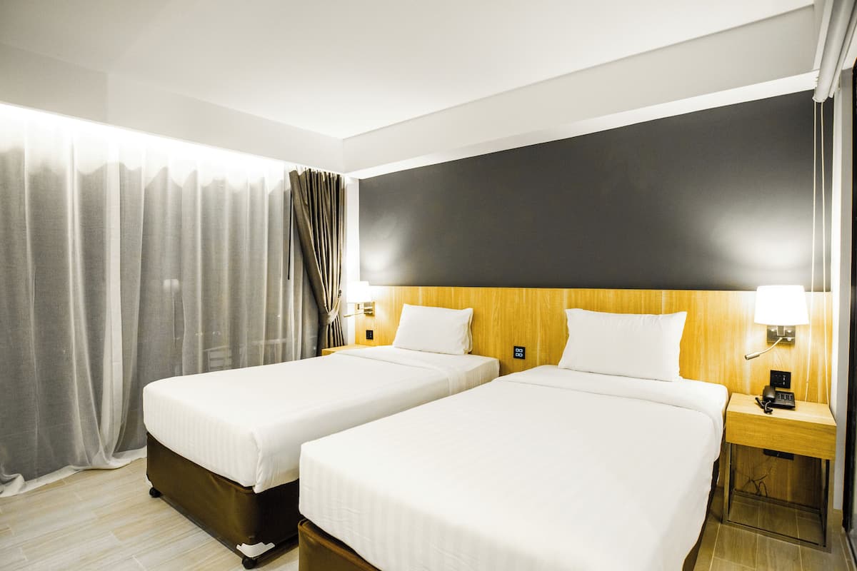 Hotelkamer met twee bedden, een grote flatscreen-tv, een houten hoofdeinde, bedlampen en een gordijn.