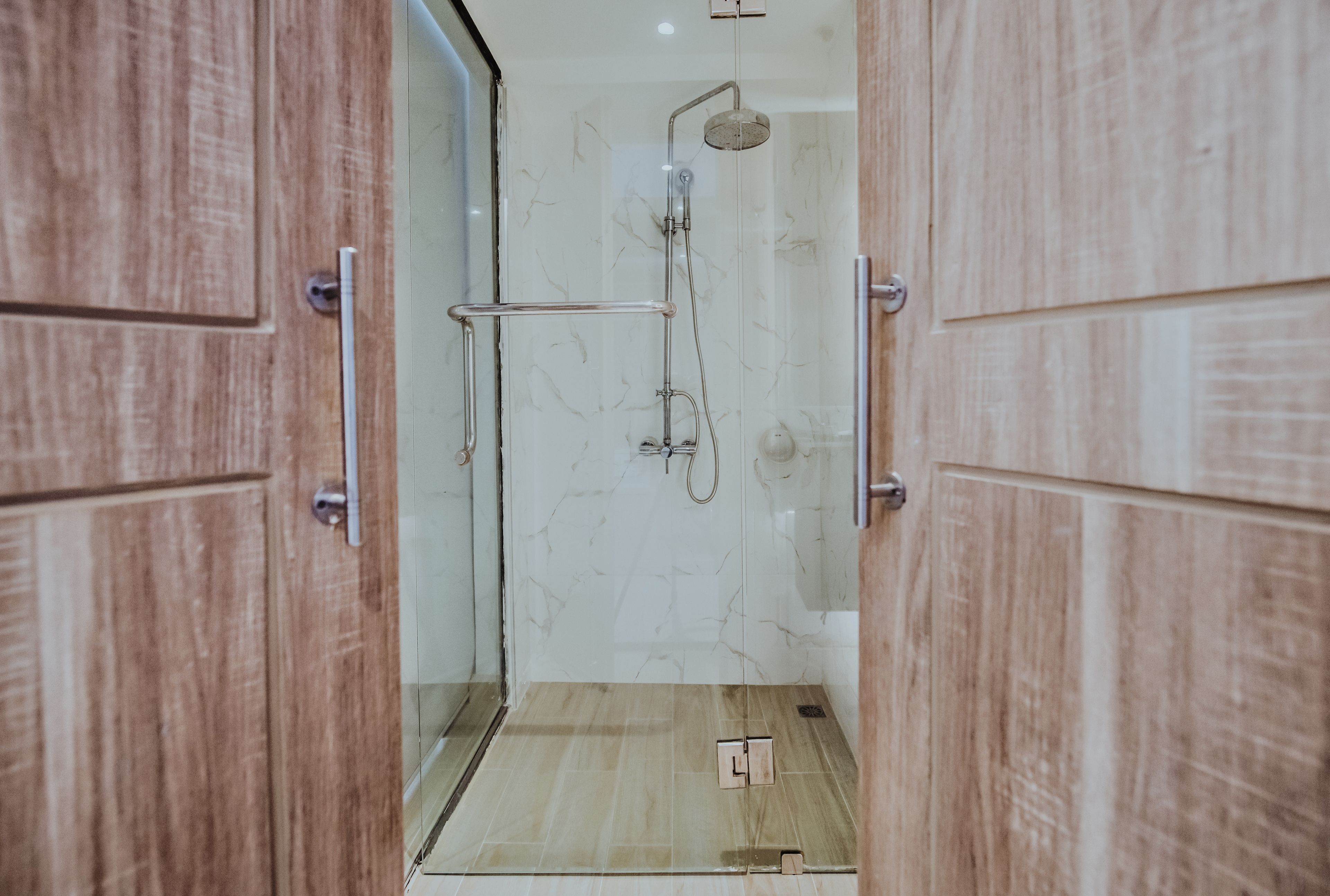 Une porte en bois donne accès à une salle de bain équipée d’une douche, d’un porte-serviettes et de toilettes.