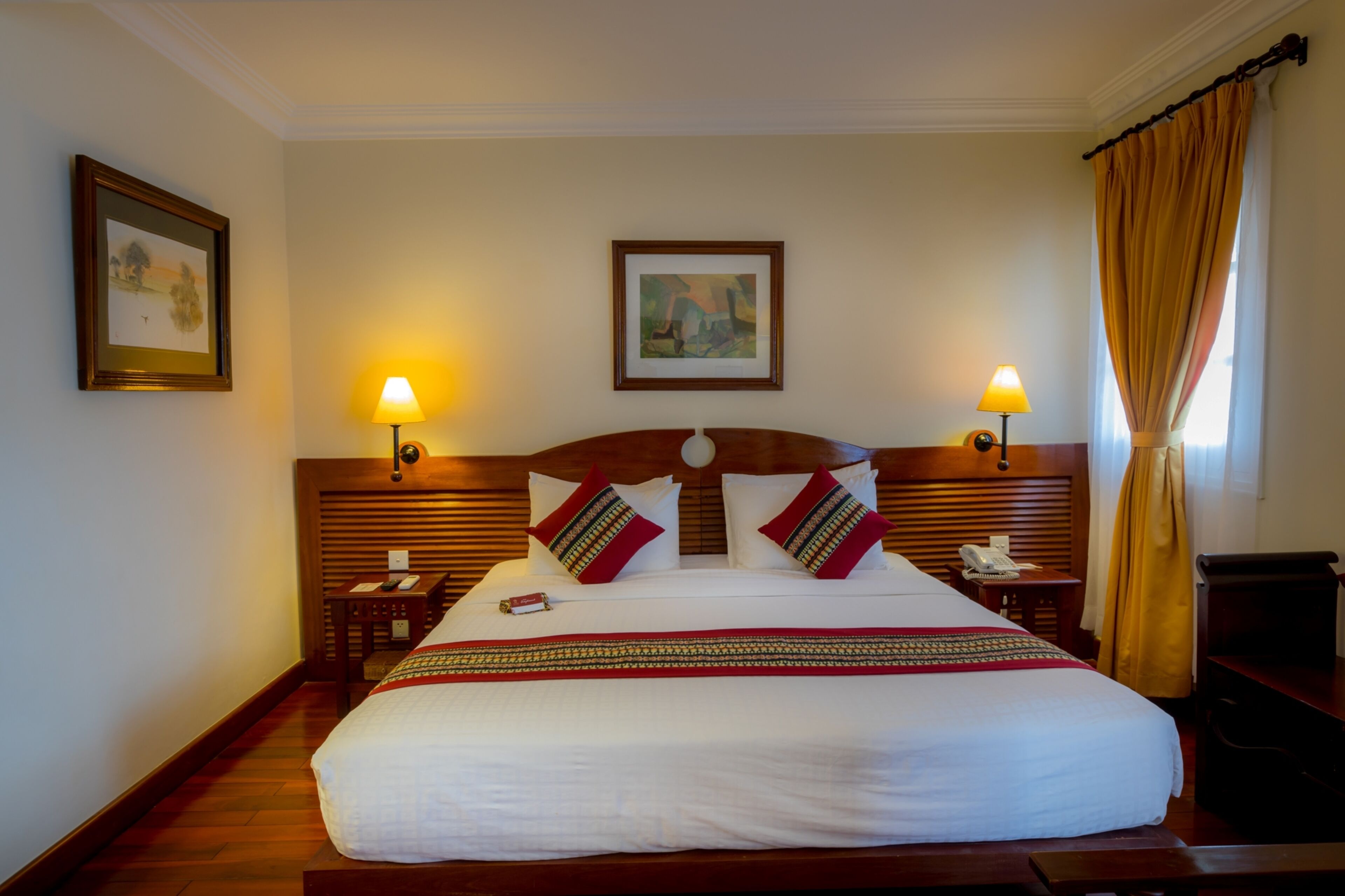 A neatly made bed with a wooden headboard, two bedside tables with lamps, and framed artwork on the walls.