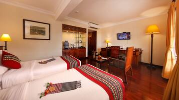 A hotel room with two beds, a desk, a chair, a television, and a dining area.