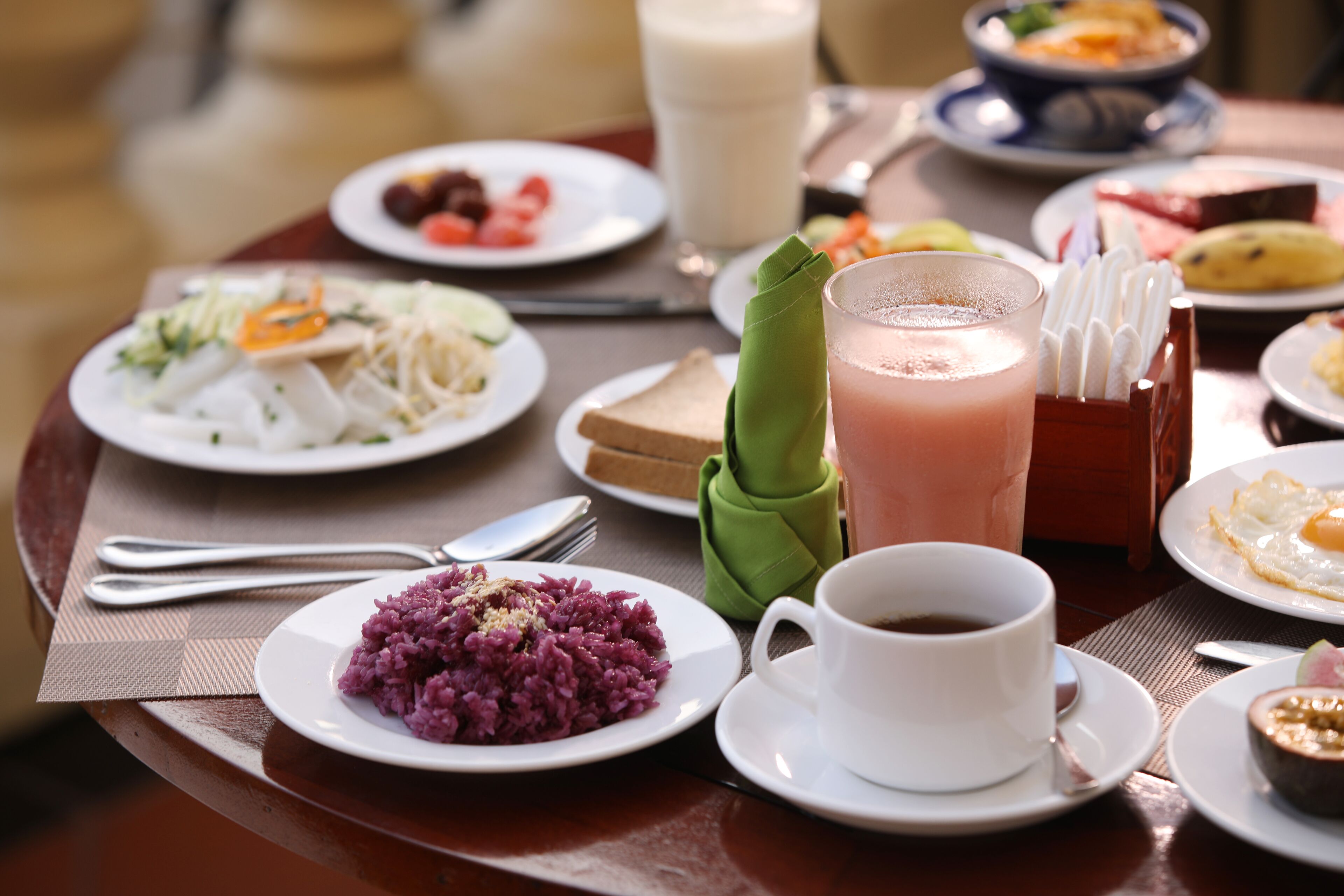 A dining table with various dishes including purple rice, toast, and a green napkin.