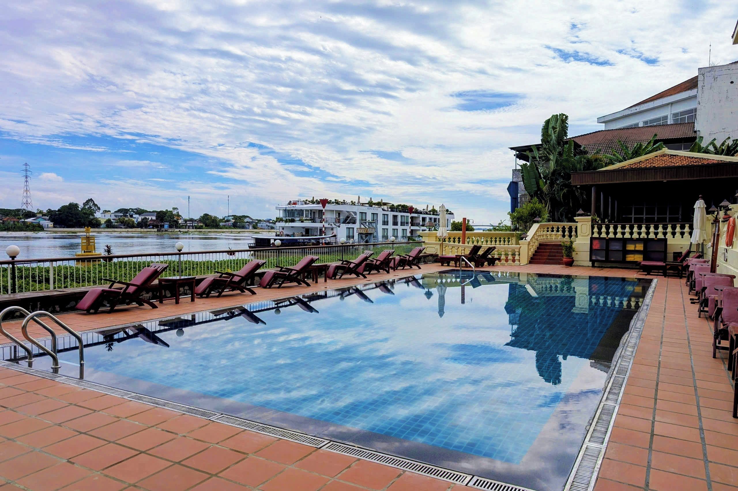 A swimming pool with lounge chairs, a view of a body of water, and a building with a balcony.
