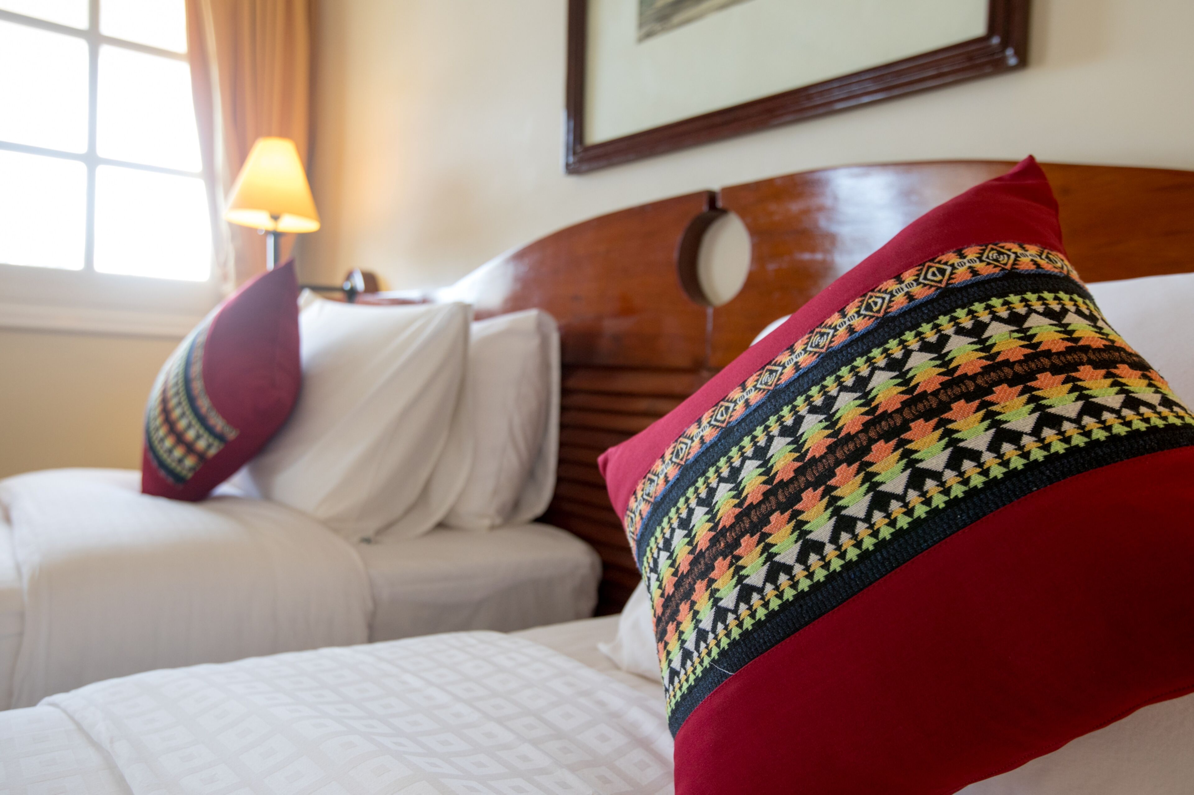 A hotel room with a wooden headboard, a bed with white bedding, and a red patterned pillow.