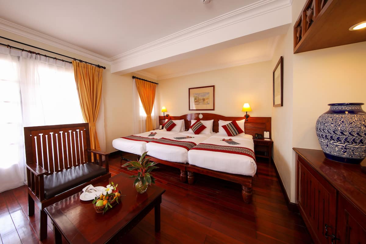 Habitación de hotel con cama doble, un banco de madera, una mesa con un florero y un florero grande azul y blanco sobre un mueble.