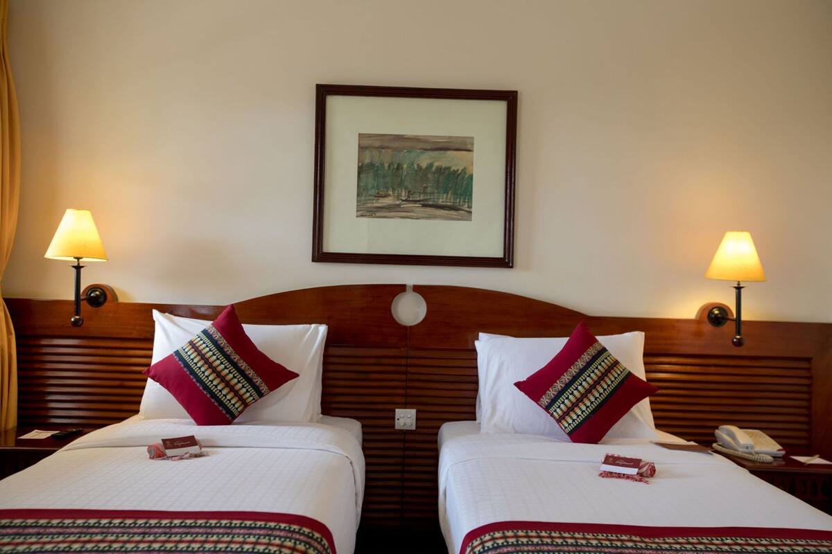 Une chambre d’hôtel avec deux lits, chacun agrémenté d’un oreiller à motifs et d’un tableau encadré au-dessus.