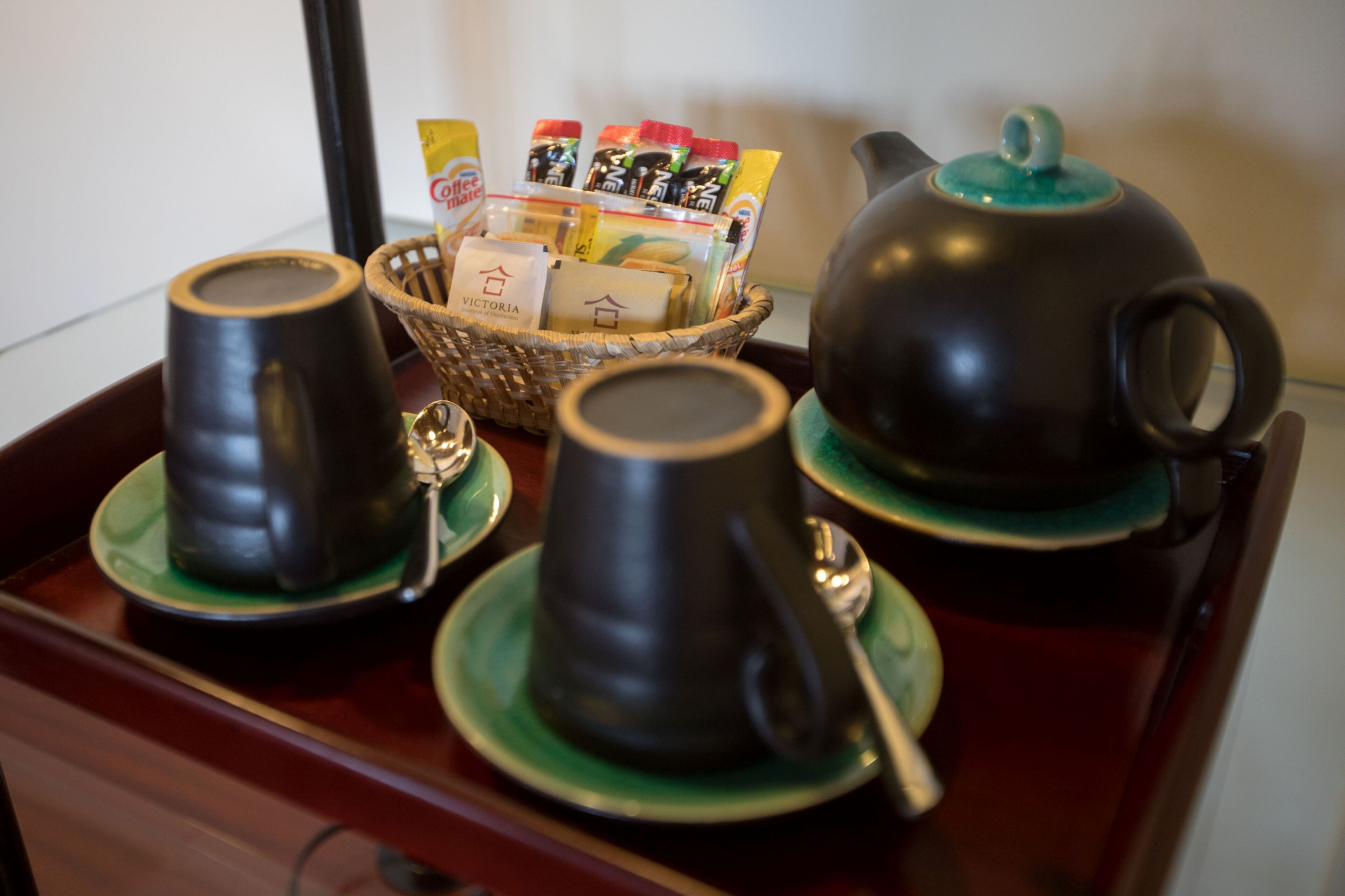 Een theeset met twee kopjes en een theepot op een dienblad, inclusief een mandje met theezakjes.