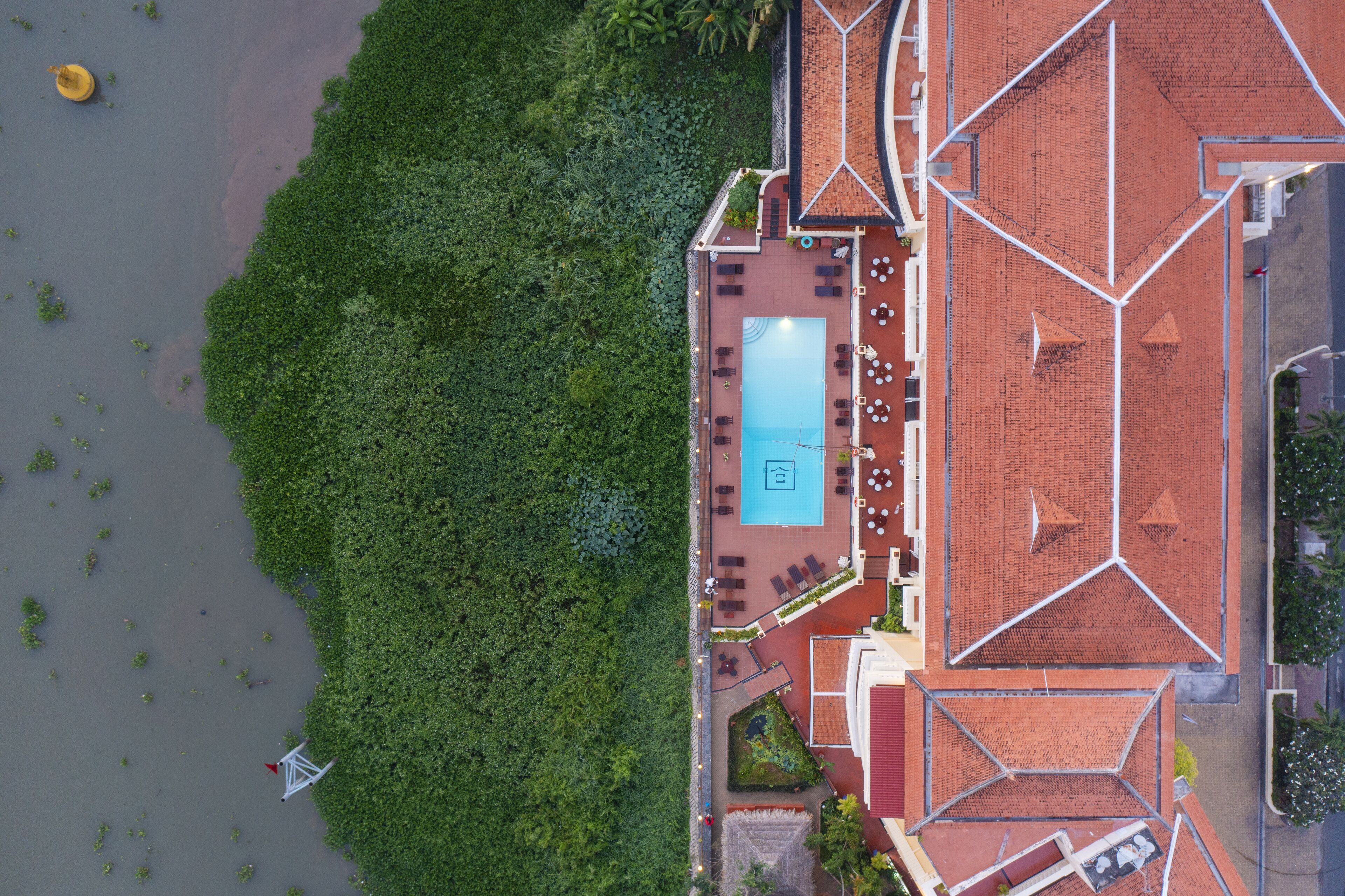 An aerial view of a hotel with a swimming pool, outdoor seating area, and a lush green landscape.