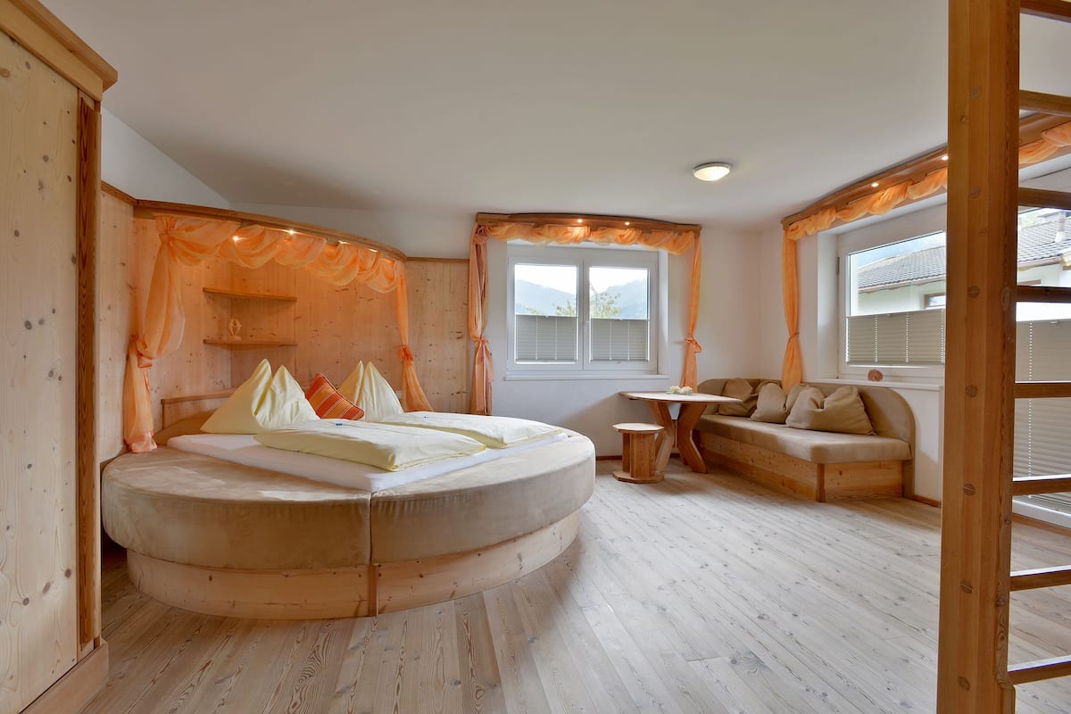 Ein Schlafzimmer mit einem runden Bett, einem kleinen Tisch, einer Couch und einem Fenster mit Vorhängen.