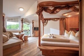 A bedroom with a canopy bed, a wooden bench, a small table, and a TV in the corner.