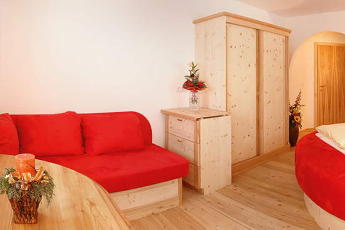 Ein Schlafzimmer mit einem roten Sofa, einem Himmelsbett, einem Holzschrank und einem kleinen Tisch mit einer Vase.