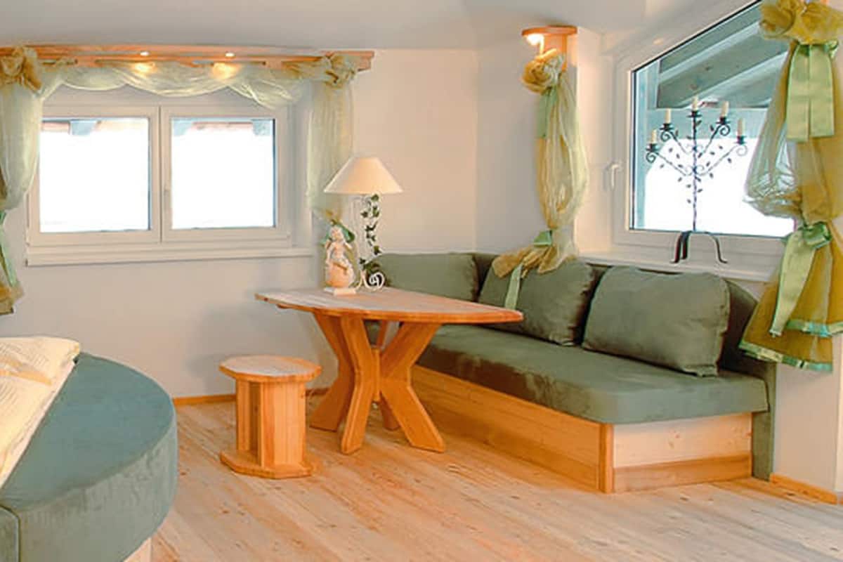 Ein gemütliches Schlafzimmer mit Bett, einem kleinen Tisch, einer Couch und einem Fenster mit Vorhängen.
