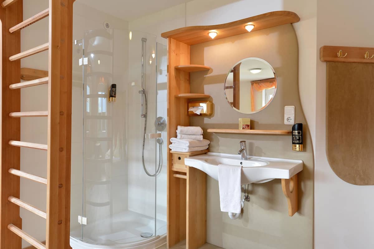 Ein modernes Badezimmer mit Duschabtrennung aus Glas, Holzregalen, einem Waschbecken und einem Spiegel.
