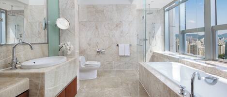 A modern bathroom with a large bathtub, a sink, and a toilet. It features a large window with a city view.