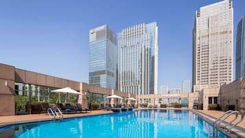 A swimming pool with lounge chairs and umbrellas, surrounded by modern high-rise buildings.