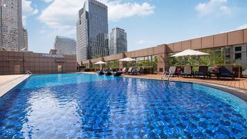 Una piscina con sillas de descanso y sombrillas, rodeada de edificios modernos.