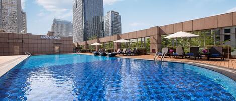 Una piscina con sillas de descanso y sombrillas, rodeada de edificios modernos.