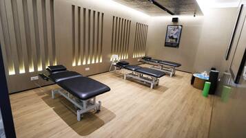 A room with three massage tables, a small table with a chair, and a poster on the wall.
