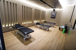 Une pièce comprenant trois tables de massage, une petite table avec une chaise et une affiche accrochée au mur.